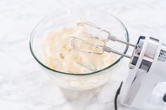 an electric hand mixer mixing cream in a glass bowl on a marble counter top,