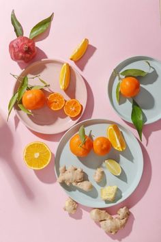 three plates with oranges, lemons and ginger slices on them sitting on a pink surface