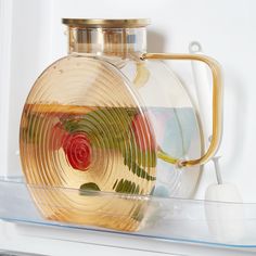 a glass container with a gold handle on top of a shelf next to a white wall