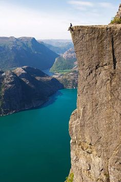 a man standing on top of a cliff next to a large body of blue water