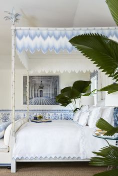 a white bed with blue and white decor in a bedroom next to a palm tree