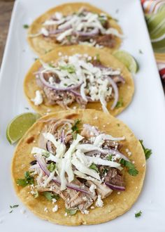 three tacos with meat, onions and cilantro on a white platter