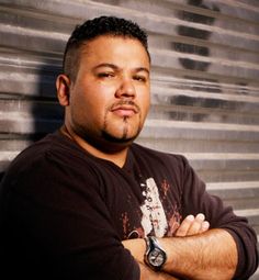 a man with his arms crossed standing in front of a metal wall and looking at the camera