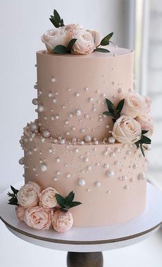 a three tiered pink wedding cake with flowers on top and pearls around the edges