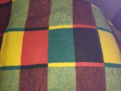 a multicolored checkered blanket on top of a bed with red, yellow and green pillows