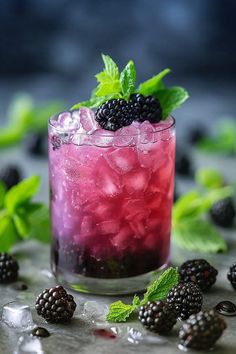 a blackberry cocktail with ice and mint garnish on a table next to blackberries