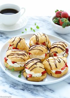 a white plate topped with pastries next to a bowl of strawberries and a cup of coffee