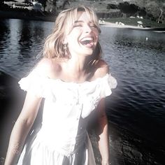 a woman in a white dress laughing by the water