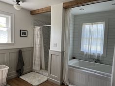 a bathroom with a tub, shower and rug on the floor in front of two windows