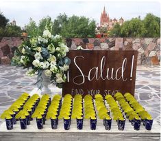 a table topped with lots of yellow cupcakes next to a vase filled with white flowers