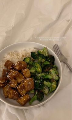 a white bowl filled with rice and broccoli covered in sauce next to a fork