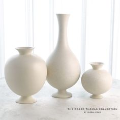 three white vases sitting next to each other on a table