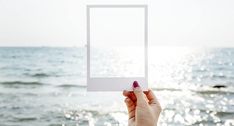 a person holding up an empty square photo frame in front of the ocean with sunlight reflecting off the water