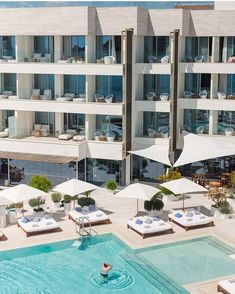 an outdoor pool with lounge chairs and umbrellas in front of a large white building