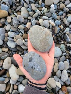 two rocks in the palm of someone's hand on a rocky beach with pebbles