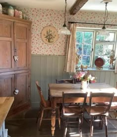 a dining room table and chairs in front of a window with flowers on the wall