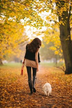 a woman walking down a leaf covered path with her dog