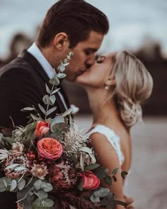 a bride and groom kissing each other in front of the camera with flowers on their bouquet