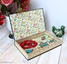 a wooden box filled with lots of colorful beads next to a green bird figurine