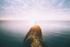 a person standing on top of a small island in the middle of the ocean at sunset