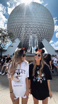 two girls standing in front of the spaceship at disney world with their heads turned to look like mickey mouse