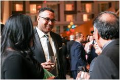 a man in a suit and tie talking to two other people at a social gathering