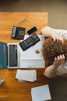 a woman sitting at a desk with her head in her hands, next to an open laptop