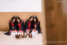 three young women sitting on the ground in front of a wall