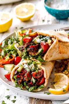 two wraps filled with meat and vegetables on a plate next to lemon wedges, rice and salad