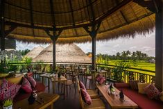 an outdoor restaurant with thatched roof and wooden tables on the balcony overlooking rice fields