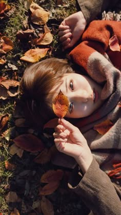 a woman laying on the ground with leaves in her hand and looking at the camera