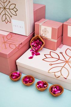 pink and gold boxes with rose petals in them sitting on a table next to each other