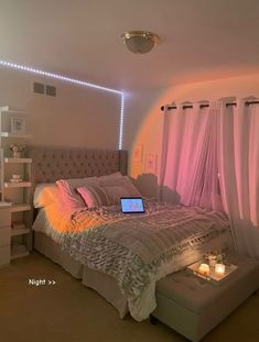 a laptop is sitting on top of a bed in a room with pink curtains and lights