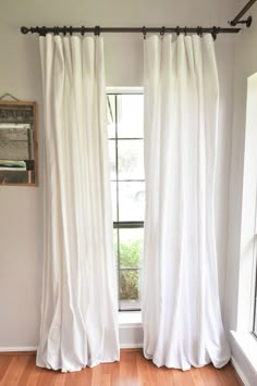 a white curtain hanging in front of a window next to a wooden floor and wall