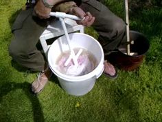 a man sitting in the grass with a bucket full of water and two shovels