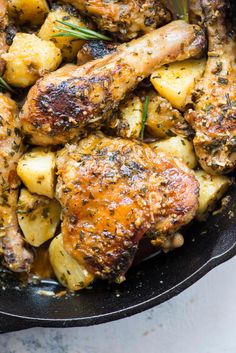 chicken and potatoes cooking in a skillet with rosemary sprigs on the side