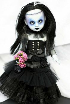 a doll with black hair and blue eyes holding a pink flower in her left hand