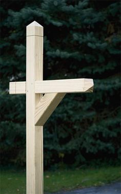 a wooden cross on the side of a road in front of some green grass and trees