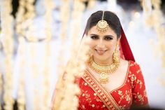 a woman in a red and gold bridal outfit smiles at the camera while she is dressed