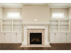 an empty living room with white bookcases and a fireplace