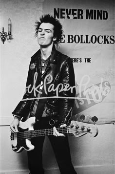 a black and white photo of a man with a guitar in front of a wall