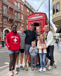 a group of people standing in front of a red phone booth on a city street