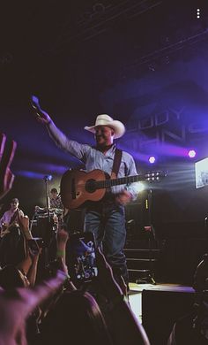 a man with a cowboy hat and guitar in front of an audience at a concert