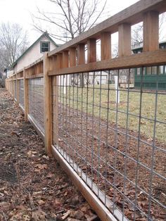 the fence is made of metal wire and has wood slats on it, along with leaves scattered all over the ground