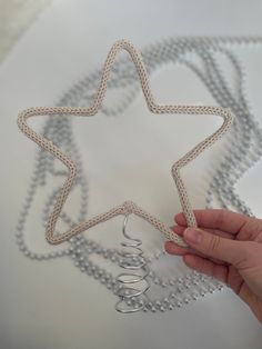 a hand is holding a star shaped object with beads on the bottom and silver chains around it