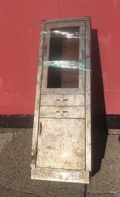 an old metal cabinet sitting on the side of a road next to a red wall