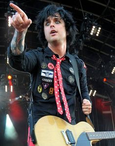 a man with black hair and red tie holding a guitar