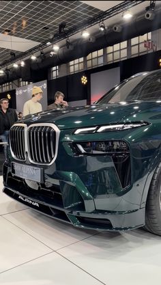 a green car is on display at an auto show with people standing around and looking at it