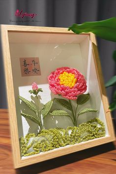 an artificial flower in a glass box with moss and flowers on the table next to it