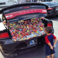 a young boy standing next to a black car with candy in it's trunk